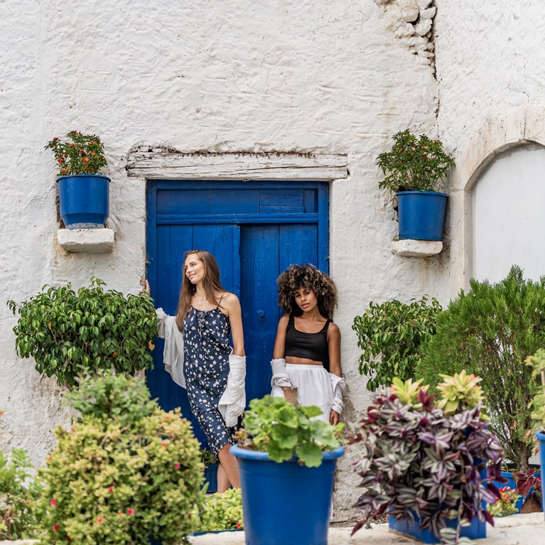 Two women standing outside white building with blue doors and greenery Hersonissos