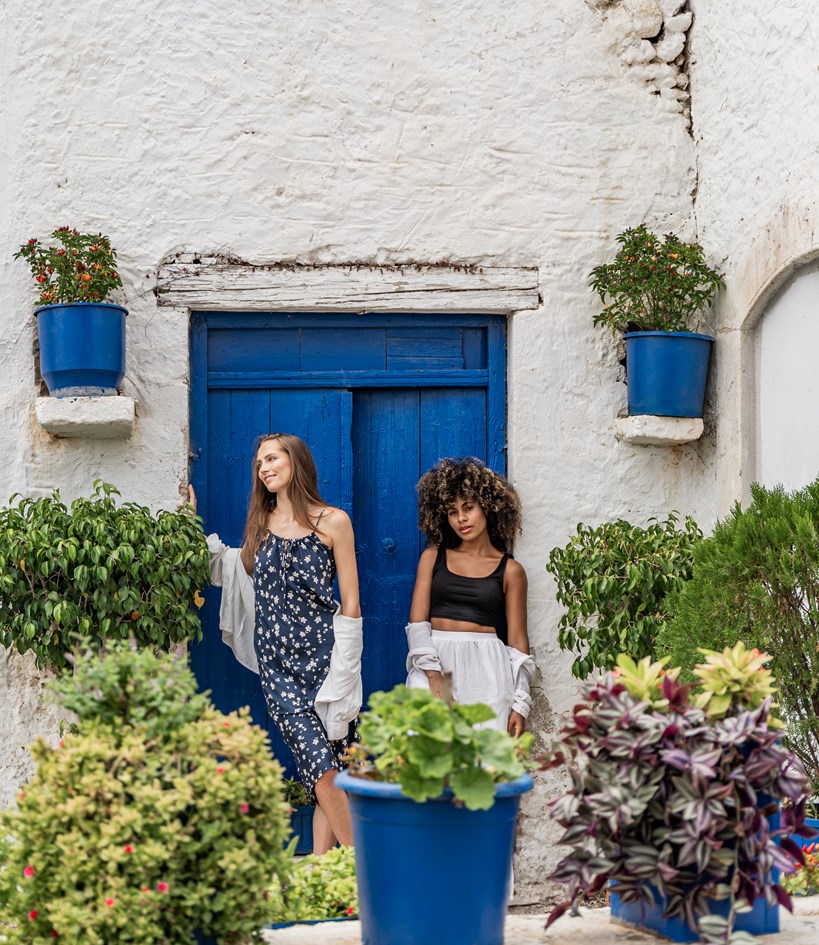 Two women standing outside white building with blue doors and greenery Hersonissos